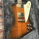 Elektrická kytara s hnědým sunburst povrchem a bílým pickguardem, umístěná v otevřeném kufru s šedou vnitřní výplní. Nástroj má dva snímače typu humb…