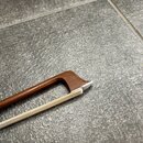 Detailní pohled na horní část hmatníku a hlavu nástroje z tmavého dřeva. K tělu je připevněna bílá struna nebo tětiva. Povrch dřeva vykazuje mírné op…