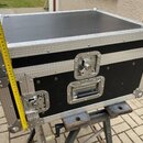 Černý transportní flightcase s hliníkovými hranami a kovovými rohy. Na přední straně jsou umístěny dvě kovové zapínací zámky a jedna madla pro přenáš…
