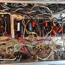 Detailní pohled do otevřeného šasi elektronického zařízení s hustou sítí barevných vodičů a komponentů. Na černé desce jsou vidět kondenzátory, rezis…