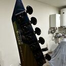 Detail zadní strany hlavy elektrické kytary v tmavě modré barvě s černými ladicími kolíky. Na povrchu jsou nápisy „Compliant with RoHS Directive“, „C…