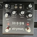 Černý kytarový pedál s nápisy IRIDIUM amp & ir cab a strymon. Zařízení má osm ovládacích knoflíků, dva přepínače v horní části s popisky AMP (round,…