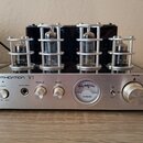 Stříbrný vakuumový zesilovač s černými bočními panely a čtyřmi elektronkami v kovových ochranných klecích. Na předním panelu jsou nápisy INTIMIDATION…