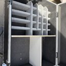Otevřený transportní case s černým povrchem a hliníkovými hranami. Horní část obsahuje vložku z šedé pěny s mřížkovým členěním pro uložení kabelů neb…
