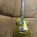 Zlatá elektrická kytara s tvarem singlecut a bílým pickguardem. Na hlavě hmatníku je bílé logo Gibson. Tělo kytary vykazuje v dolní části výrazné hor…