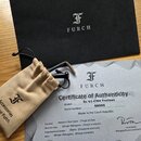 Fotografie zobrazuje certifikát pravosti, textilní vak a černou obálku s logem FURCH. Na certifikátu je uveden model Bc 61-CM4 Fretless, sériové čísl…
