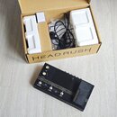 Černý kytarový procesor s nápisem HEAD RUSH a FLEX PRIME. Zařízení má několik ovládacích knoflíků, tlačítka s popisky STOMP/RIG, LOOPER a TUNER a pra…