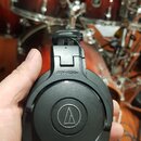 Černé uzavřené sluchátka s nápisem ATH-M30x a logem značky Audio-Technica v kruhu. Povrch plastu vykazuje drobné známky používání a lehké znečištění.…