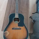 Akustická kytara v provedení dreadnought s barevným přechodem od černé k hnědé (sunburst). Na těle je černý plechtr zaštrčník a v místě spodního rohu…