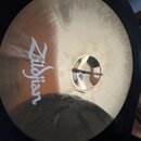 Kruhová mosazná činely s viditelným broušením povrchu. Na levé straně je bílý nápis Zildjian. Uprostřed se nachází otvor, v němž je vidět část černéh…