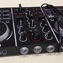 Černý DJ kontrolér s dvěma stříbrno-černými jog-koly. Na přístroji jsou viditelné nápisy Numark a PARTY MIX. Zařízení obsahuje řadu ovládacích knoflí…
