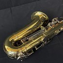 Detailní pohled na zlatý lakovaný saxofon z horní strany. Na trubici je vyryt nápis "YAMAHA". Povrch nástroje je vysoce lesklý s viditelnými odlesky.