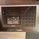 Stříbrný sampler MPC s černým ovládacím panelem. Na zařízení jsou nápisy AKAI PROFESSIONAL, MPC LIVE II a STANDALONE MUSIC PRODUCTION CENTER. Obsahuj…