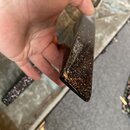 Detailní pohled na hranu hudebního nástroje s tmavým, třpytivým povrchem v hnědo-černé barvě. Povrch je vysoce lesklý a hladký bez viditelných poškoz…
