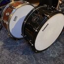 Na fotografii jsou dva basové bubny. Levý je v dřevěném provedení s nápisem TAMA, pravý je černý s logem MAPEX a membránou značky EVANS. Oba nástroje…