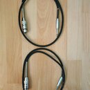 Dvě černé audio kabeláže s konektory typu XLR na jedné straně a 6,3mm jack na straně druhé. Konektory jsou vyrobeny z kovového materiálu stříbrné bar…