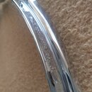 Detailní pohled na chromovaný kovový obruč (hoop) z bubnu. Na povrchu je vyryt nápis „Pearl SuperHoop“ doprovázený logem značky. Povrch je hladký a v…