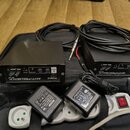 Na černé podložce leží dvě identické černé kovové krabičky s nápisy Roland ANTI-FEEDBACK. Každý přístroj má na předním panelu ovládací prvky s popisk…