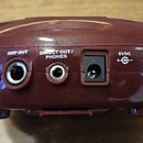 Záběr na zadní panel vínového plastového zařízení s několika konektory. Jsou zde vidět nápisy CD/MP3 IN, AMP OUT, DIRECT OUT / PHONES, 9VDC +C- a GUI…