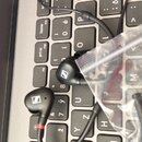 Černé intraaurální sluchátka s kabelem položená na šedé počítačové klávesnici. Na obou sluchátkách je viditelné bílé logo znacky Sennheiser. Jeden z…