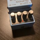 Modrý efekt pedál s nápisy SUPER Chorus a CH-1. Na horní části je černý gumový spínač s logem BOSS, které je zobrazeno obráceně. Na předním panelu js…