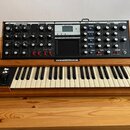 Černý analogový syntetizátor s dřevěným šasi a klaviatuрой. Na horním panelu jsou vidět nápisy LFO, MODULATION BUSSERS, OSCILLATORS, MIXER, FILTERS,…