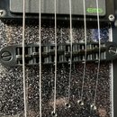 Detailní pohled na černý most sádlou elektrické kytary. Nad mostem je viditelný černý snímač s nápisem EMG v zelené barvě. Tělo kytary má tmavý povrc…