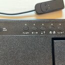 Detailní pohled na ovládací panel černého zařízení s texturovaným povrchem. Na panelu se nachází tlačítko s nápisem LED on/off a pět kulatých tlačíte…