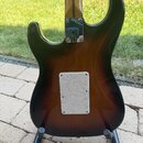 Zadní strana elektrické kytary s barevným přechodem od černé k hnědé (sunburst). V horní části je kovová krytka s nápisem CE a v dolní části bílý per…