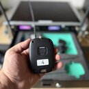 Ruka drží černý bezdrátový vysílač s anténou. Na zařízení je bílý nápis SHURE a pod ním označení modelu SLXD1. Ve spodní části je nalepený bílý štíte…