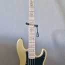 Zlatá elektrická basová kytara s černým pickguardem a světlou hmatníkem. Na hlavě je nápis Fender PRECISION BASS. Nástroj je umístěn na černém stojan…