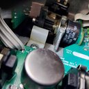 Detailní pohled do vnitřku elektronického zařízení s viditelnou zelenou základní deskou a zapojenými komponenty. Na černém potenciometru je bílý nápi…