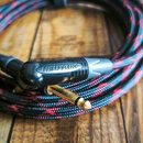 Černý instrumentální kabel s červeně propleteným textilním opletením. Na černém plastovém konektoru je bílý nápis NEUTRIK a zlatý 6,3mm jack konektor…