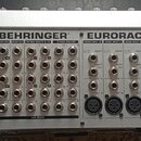 Zadní strana stříbrného mixážního pultu s nápisem BEHRINGER EURORACK MX 2642A. Zařízení obsahuje řadu vstupních a výstupních konektorů, včetně XLR, j…