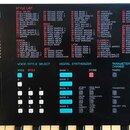 Detailní záběr na ovládací panel digitálního syntetizátoru s nápisem DIGITAL SYNTHESIZER. V horní části je tabulka STYLE LIST rozdělená do kategorií…