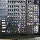 Černý mixážní pult s modrými a bílými prvky. Na panelu jsou nápisy Professional Audio, Quality Mix, VX-2442 a 24 Channel Mic/Line Mixer. V pravém hor…