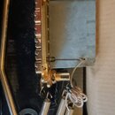 Detailní pohled na kovové součástky v černém instrumentu. Je vidět zlatý kovový mechanismus s ozubeným prvkem a přilehlý matně stříbrný kovový blok.…
