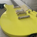 Žlutá elektrická kytara s tvarem typu Les Paul. Nástroj má dva humbuckery, stříbrný most a ladicí mechanismy. Povrch je hladký a glossy, bez viditeln…