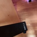 Detailní pohled na černý, hranatý konec hudebního přístroje nebo příslušenství. Na boku je bílým písmem uveden nápis DUO 2.2. Povrch vykazuje drobné…