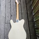 Zadní strana elektrické kytary s bílým korpusem a světlým dřevěným hnedem krku. Kytara má tvar připomínající model Telecaster a je vybavena kovým kry…