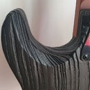 Detail zadní strany korpusu elektrické kytary v černé barvě. Povrch má výraznou, hluboko vyrytou strukturu imitující zrnitost dřeva. V pravé části je…