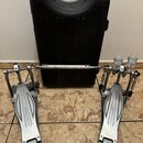 Dvojpedál na bubny stříbrné barvy s černým kufrem v pozadí. Na obou pedálech je nápis speedcobras a na špičkách logo IZAMA. Na spojovací tyči je rovn…