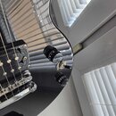 Detailní pohled na černý lesklý povrch elektrické kytary. Jsou vidět dvě černé oválné potenciometry s bílým číslováním a jeden přepínač s nápisem "RH…