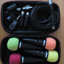 Otevřený černý kufřík s příslušenstvím pro mikrofony. V horní části je smotaný černý kabel, černý mikrofon, USB kabel a tři černé bezdrátové vysílače…
