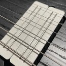 Detailní záběr na bílý snímač elektrické kytary s viditelnými slítinami pólů. Snímač je osazen v černém těle kytary s výraznou strukturou dřeva. Na p…