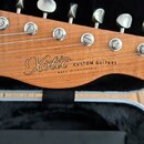 Detail hlavy elektrické kytary z dřeva s viditnou kresbou. Na dřevě je vyryt nápis Xotic CUSTOM GUITARS a pod ním menší text MADE IN CALIFORNIA. Na h…