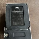 Fotografie zachycuje zadní stranu černého efektpedálu v bílém rámu. Na černé štítku je uveden nápis DC IN 9V a japonský text, ve kterém je zmíněna zn…