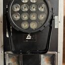 Černý LED reflektor s kruhovým uspořádáním deseti světelných prvků, umístěný v transportním kufru. Na černém povrchu pod přístrojem je vidět část bíl…