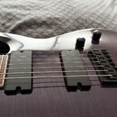 Detail elektrické kytary s fialovým lakovaným povrchem s viditnou strukturou dřeva. Nástroj má dva černá humbuckery, černý most s ladicími šroubky a…