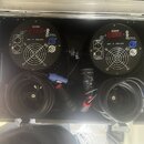 V otevřeném transportním kufru jsou umístěny dva identické černé kulovité přístroje s ventilátory a digitálními displeji. Na obou je nápis "SGM" a ov…